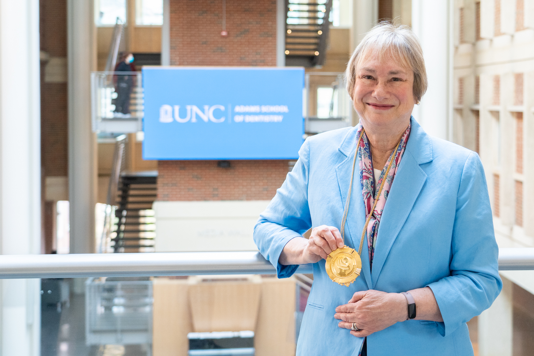 Woman in blue jacket holds up golden medal.